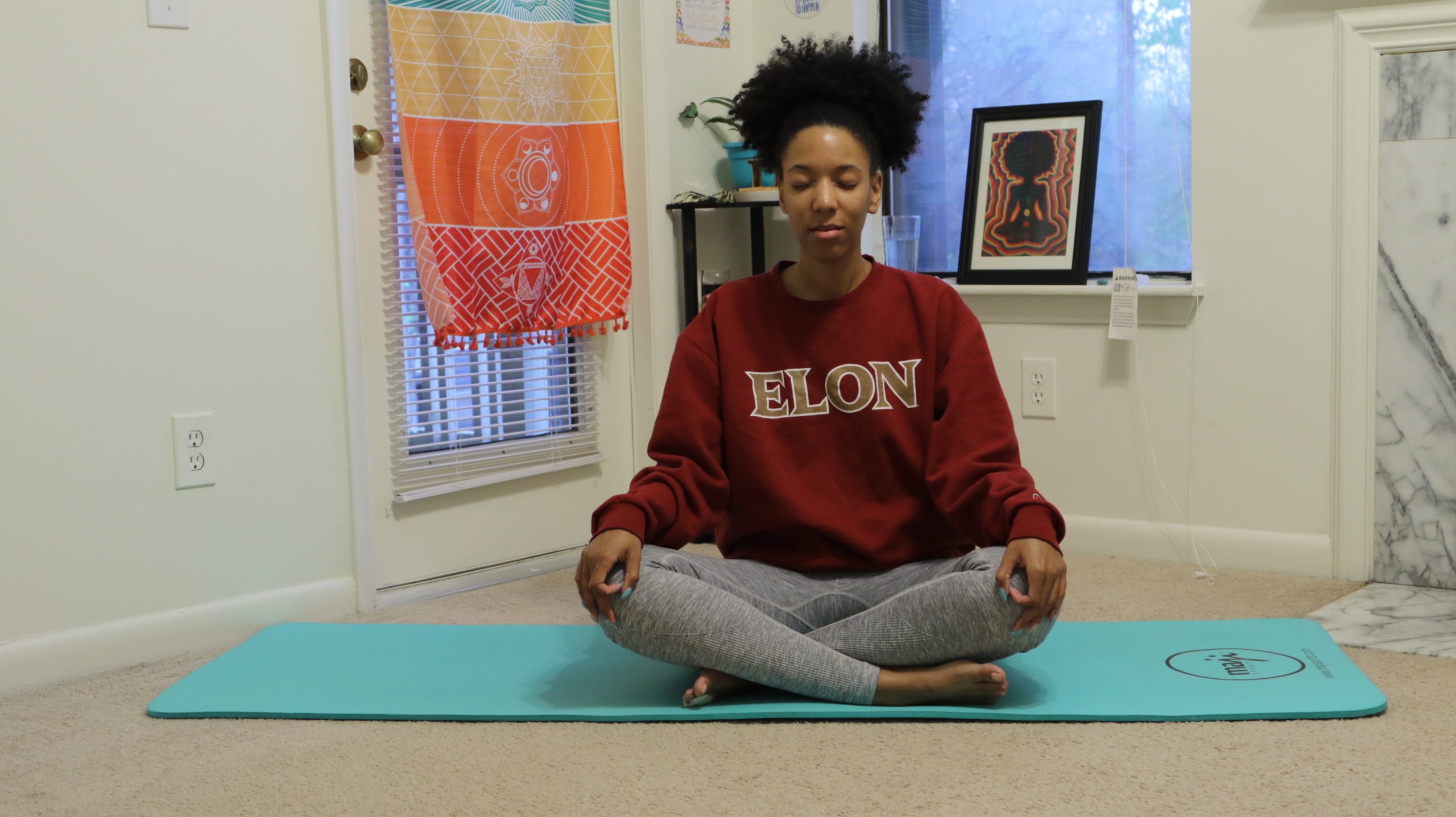 Melly sitting with legs crossed and eyes closed meditating on yoga mat